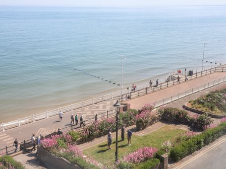 A seaside promenade with people walking and a garden with pink flowers by the sea at Fishermans Watch in Bridlington
