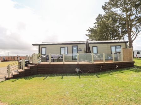 A single-story cabin with glass railing and wooden deck on a grassy area at Beechwood Lodge in Hasguard Cross near Broad Haven