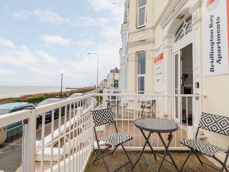 A balcony with a small table and two chairs overlooking a street and the sea at 3 Seaview @ Bridlington Bay in Bridlington