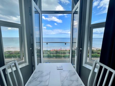A dining table with two chairs next to open windows overlooking the sea at 5 Seaview @ Bridlington Bay in Bridlington