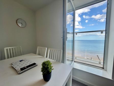 A dining area with a white table and chairs next to an open window showing a sea view at 6 Seaview @ Bridlington Bay in Bridlington