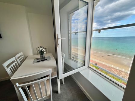 A dining area with a white table and chairs next to an open window overlooking a beach at 7 Seaview @ Bridlington Bay in Bridlington