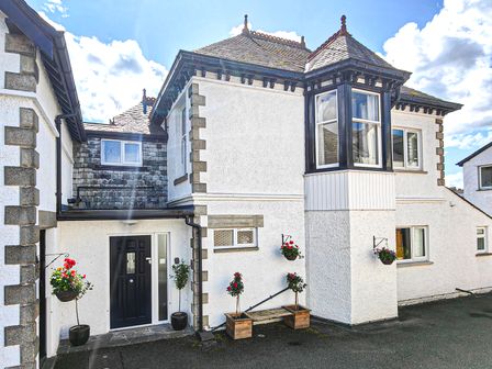 Exterior view of a white house with black trimmed windows and door with hanging flower baskets at The Paddock in Keswick