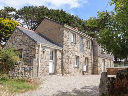 A stone exterior of a house with white doors and windows surrounded by trees at The Old Barn in St Just