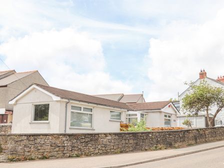 A single-story house with pebble dash walls and tiled roof behind a low stone wall with a tree at Apple Tree Bungalow in Lanner