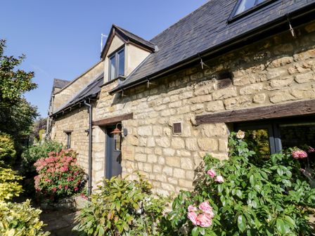 Exterior view of a stone house with flowers and plants along the wall at The Old Stables in Chipping Campden