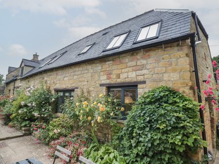 A stone house with black framed windows and plants growing along the wall at The Old Brewhouse in Chipping Campden