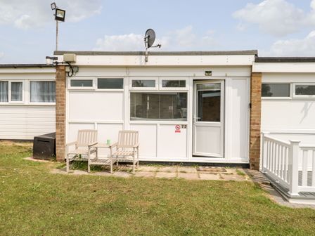 A small white building with two chairs and a table in front on a grassy lawn at 72 Hemsby