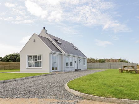 A white house with a gravel driveway and green lawn with wooden picnic tables at The Haven in Falcarragh County Donegal