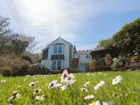 A garden with daisies in front of a two story house with a patio and outdoor seating at Glenside House in Carbis Bay