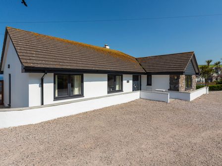 A white single story house with dark roof tiles and gravel driveway at Ocean View in Hope Cove