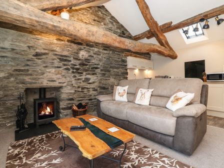 A living room with a stone wall wooden beams sofa with animal print cushions a wood burning stove and a wooden coffee table at Spinners Loft in Hawkshead