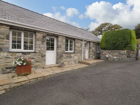 Stone building with two white doors and windows with flower planter outside and trimmed bush at Bwythyn Yr Wyddfa Llanberis