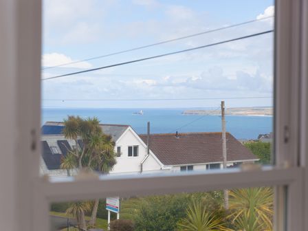 A coastal view through a window showing houses palm trees power lines and the sea at Samphire in Carbis Bay