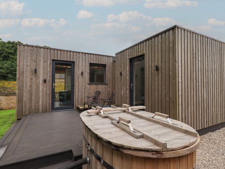 A wooden deck area with two metal chairs outside a cabin with vertical wooden panels and glass doors at Brow Wood Cabin in Ullswater