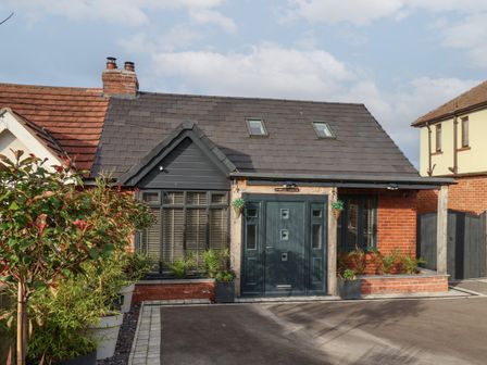 A single story house with a dark roof dark door and potted plants outside at The Dollhouse in Cayton Bay