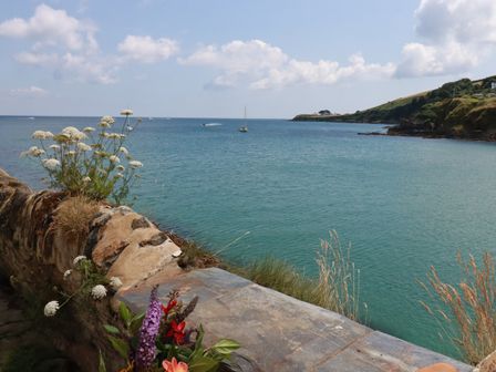 A coastal view with flowers on a stone wall overlooking the sea at Chy Rani in Portmellon near Mevagissey