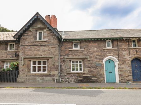 A stone cottage exterior with windows and a teal door by a roadside at Yewtree Cottage in Defynog near Sennybridge