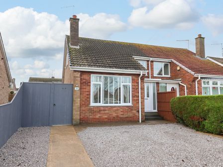 A semi detached brick house with a gravel driveway a grey gate and hedge at The Coastal Hideaway in Hornsea
