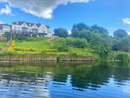 A large white house on a hill with a grassy lawn and trees by a body of water at Riverside Manor in Evesham