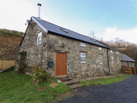 A stone house with multiple small windows a wooden door and a chimney on a grassy plot at Collfryn in Mallwyd