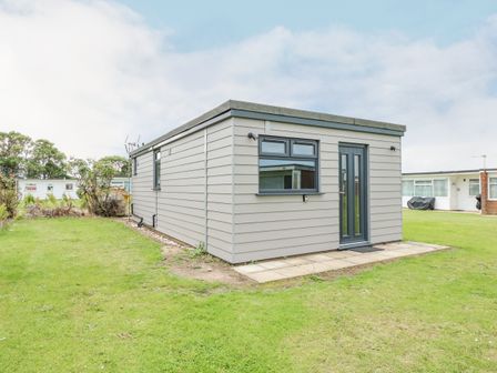 A single-story gray building with a door and window on a grassy lawn at Number 9 in California Norfolk