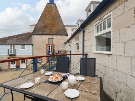 An outdoor balcony with a table set with plates cups a teapot and pastries with buildings in the background at Spindrift Brewers Quay Harbour