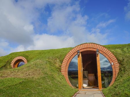 A grass-covered house with a round door and window under a blue sky at Hares View in Rhayader