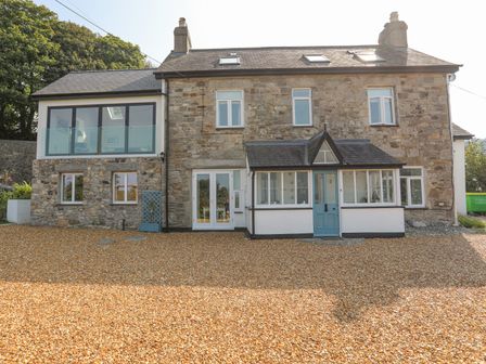 Stone house with multiple windows a blue front door and gravel driveway at Gorphwysfa in Llanddona near Beaumaris
