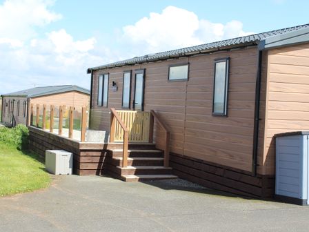 A wooden mobile home with stairs and a glass railing on a paved driveway at Sandy Bay Retreat in Hasguard Cross near Broad Haven