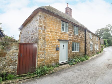 Stone cottage with thatched roof and white door along a narrow road at Wayside Stoke Abbot near Beaminster