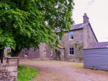An exterior view of a stone house with multiple windows a large tree and a gray shed at The Grange in Goathland