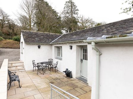 A patio area with a metal table and chairs and a bench outside a white building at The Bothy in Newby Bridge