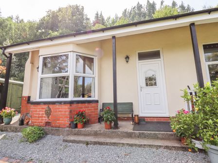 A house entrance with a white door two black support posts plants and flowers around with a gravel pathway at Trem Y Don in Dolgarrog