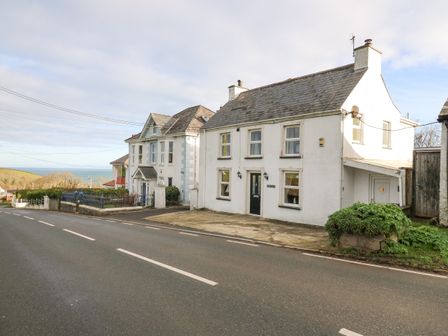 A street view of white houses by the road with a view of the sea in the background at Towyn Hall in New Quay