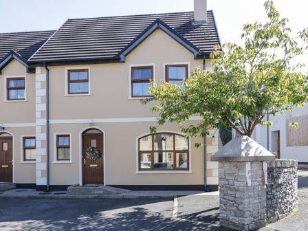 The exterior of a beige two-story house with brown doors and windows a small tree next to a stone wall at Owen Tucker View House in Ardara County Donegal