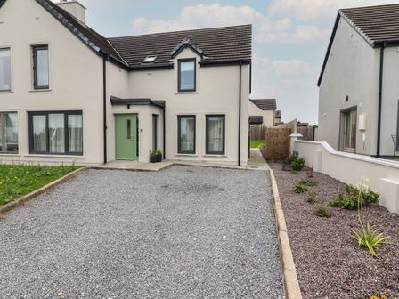 The exterior of a semi detached house with a gravel driveway a green front door and a garden bed at 19A Lighthouse Village Fenit County Kerry