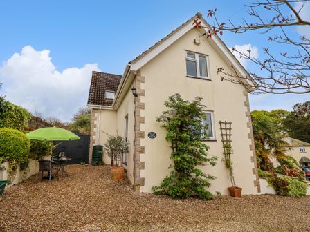Exterior of a two story house with beige walls and stone corner details a gravel yard a green umbrella with outdoor furniture and plants at Penny Corner in Whitchurch Canonicorum