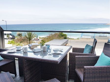 An outdoor patio with a wicker table and chairs set for a meal overlooking the ocean at Apartment 3 Fistral Beach in Newquay