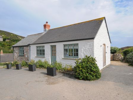 A white cottage with a grey roof and green windows with plants in black pots outside at Pendower Cottage in Porthgwarra
