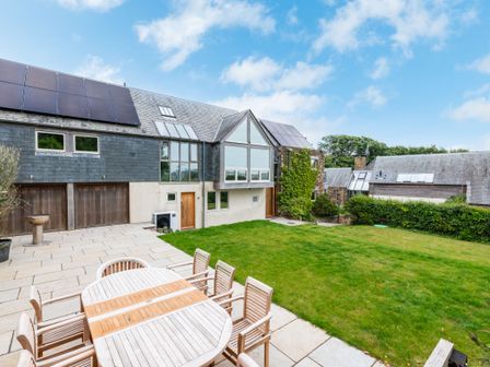 A backyard with a wooden dining table and chairs on a stone patio and a modern house with solar panels on the roof at Gull Rock 4 in Rock
