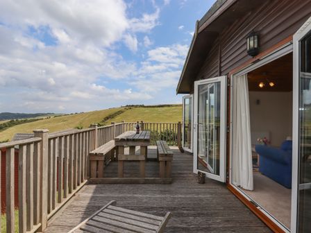 A wooden deck with a picnic table and benches overlooking grassy hills at Tamar View Lodge in Millbrook