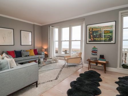 A living room with grey sofas colorful cushions a beige armchair and a glass coffee table at 42 Crag Path in Aldeburgh