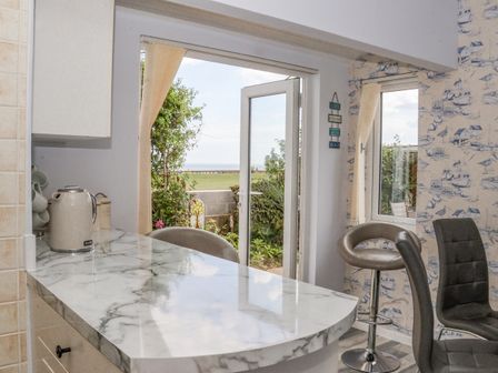 A kitchen area with a marble countertop kettle chairs and an open door leading to a garden with a view at Wavecrest in Hornsea