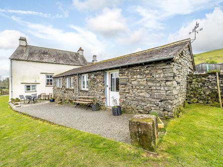 An exterior view of a stone and white painted cottage with outdoor seating on a gravel patio at Shepherds Cottage in Hawkshead
