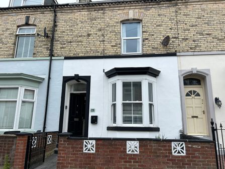 Front view of a brick terraced house with a white and black entrance and bay window at Rockton House Whitby