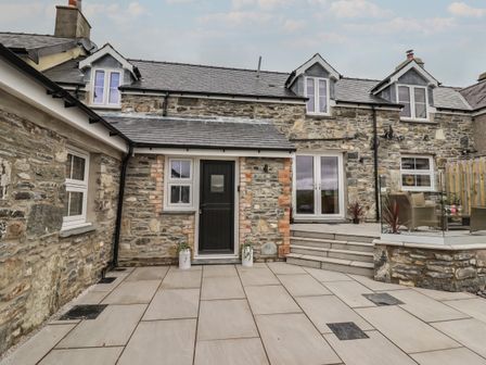 Stone exterior of a house with a black door, white windows, and a patio with steps and outdoor seating at Rhos Las in Cerrigydrudion