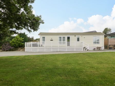 A single story mobile home with a white railing and green lawn in front at Gwel Eryri in Penmynydd near Llanfairpwllgwyngyll