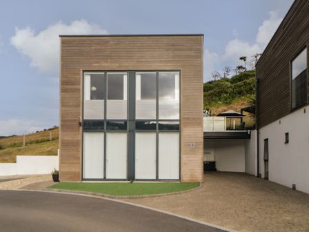 A modern two-story house with large windows and wood paneling at 12 Beachdown in Challaborough