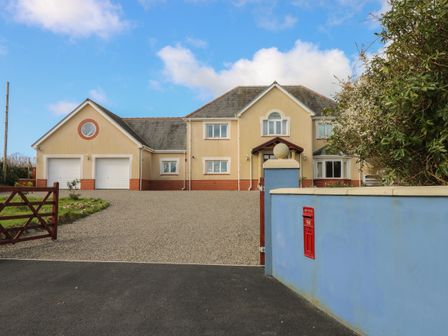 A large house with a gravel driveway two garage doors and a blue wall with a red post box at The Annexe Meadow Croft in Haverfordwest